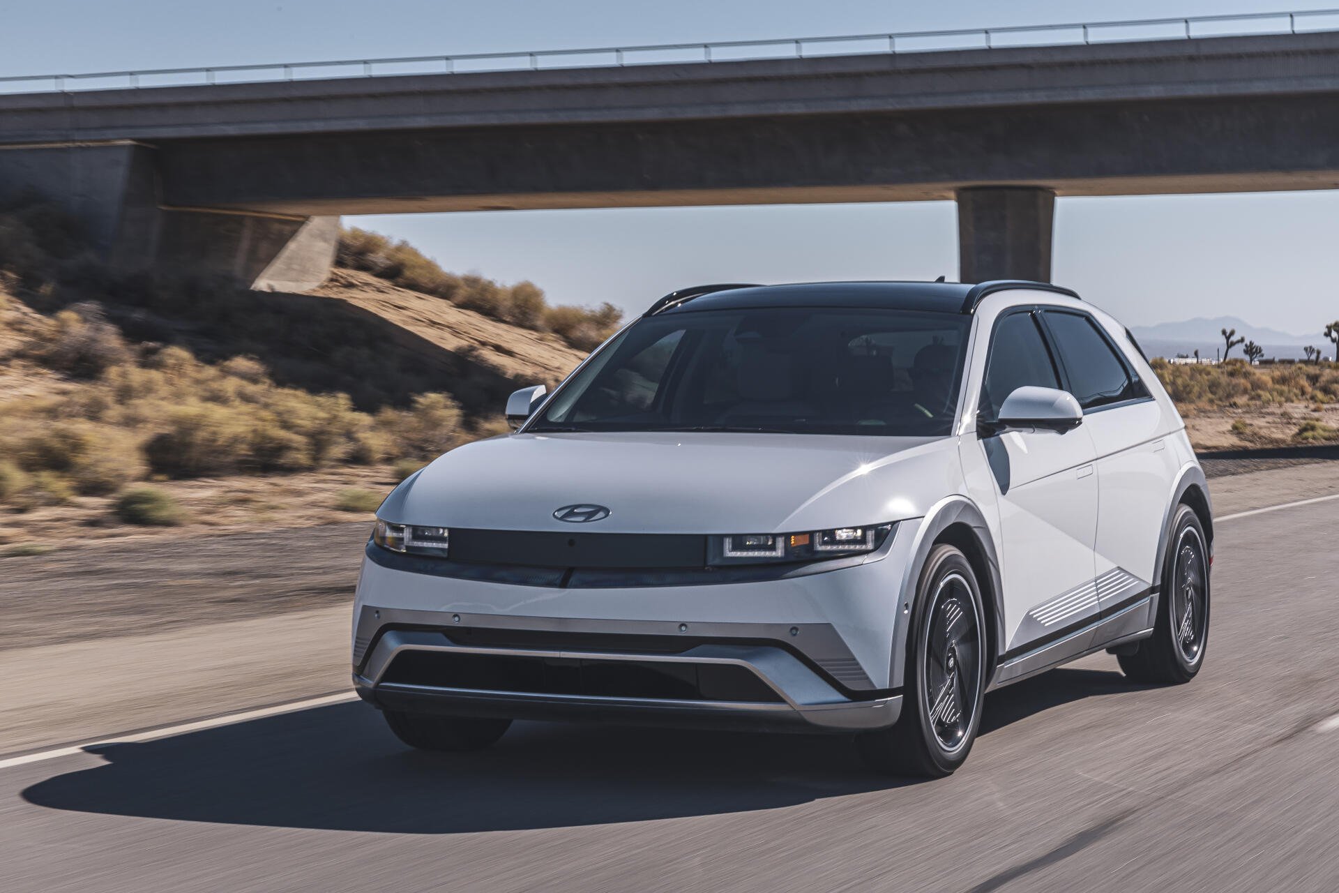 A sleek white Hyundai IONIQ 5 drives along a highway under a bridge, showcasing its modern design. This image serves as a sharp 4K Ultra HD desktop wallpaper.