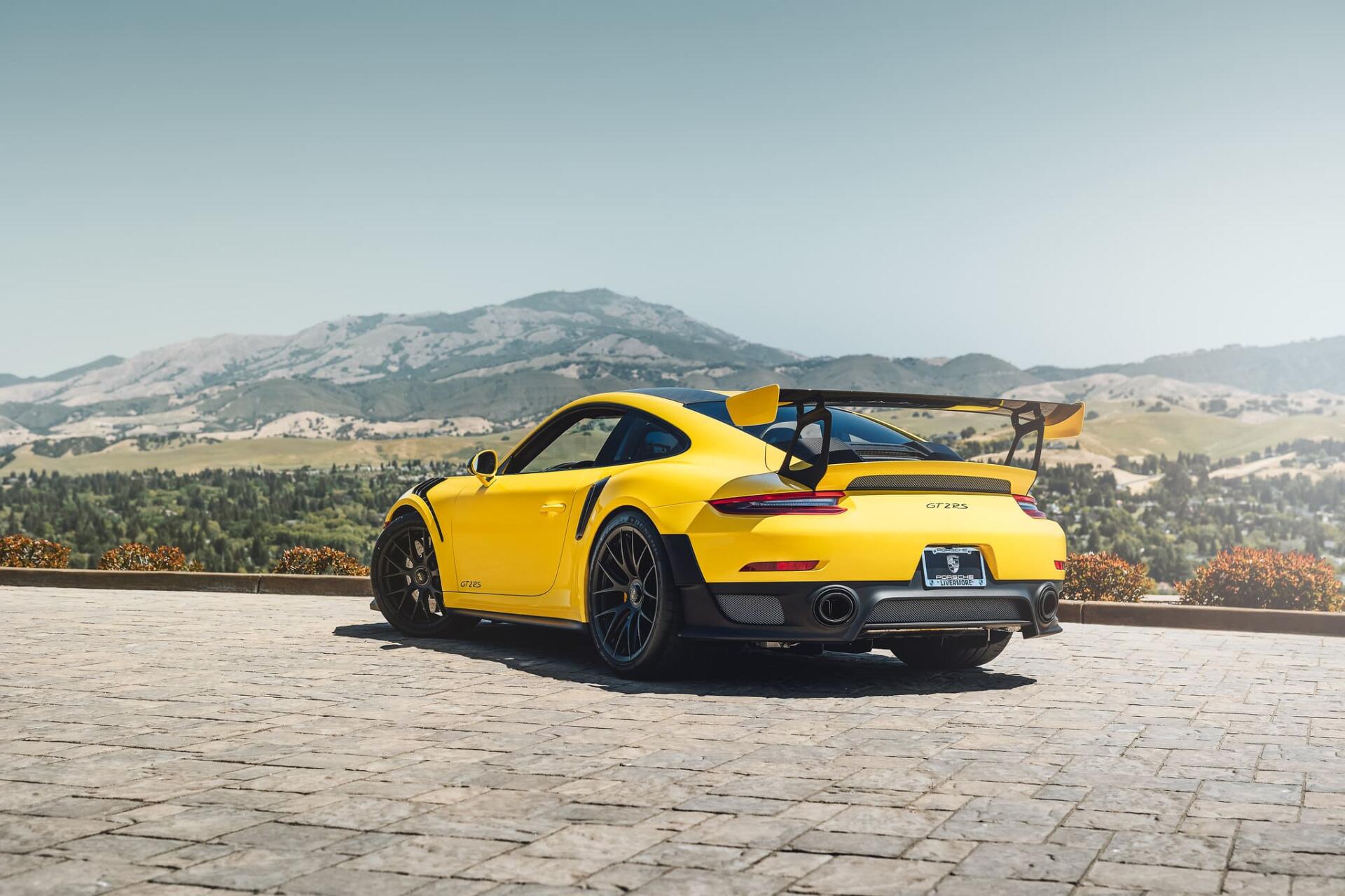 Yellow Porsche sports car rear three-quarter view parked on a mountain overlook, scenic valley and peaks in the background — HD PC desktop wallpaper and background.