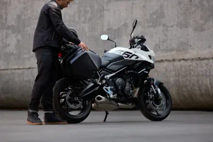 A rider adjusts the Triumph Tiger Sport 660 motorcycle, showcasing its sleek design against a textured concrete background in this 4K Ultra HD wallpaper.