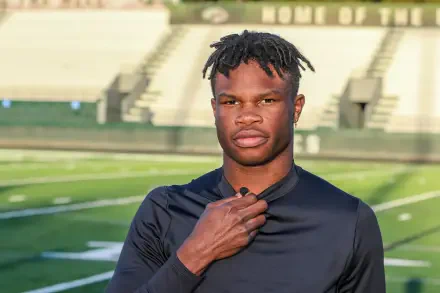 Travis Hunter poses confidently on a football field, wearing a black athletic shirt. This striking image serves as a dynamic 4K Ultra HD desktop wallpaper and background.