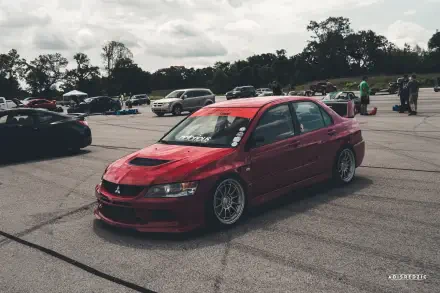 Red Mitsubishi Lancer Evolution IX parked on tarmac at a car meet, photographed as a 5K Ultra HD PC desktop wallpaper/background.