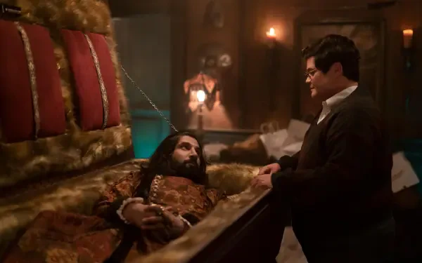A scene from the TV show What We Do in the Shadows, featuring a humorous interaction between a vampire in a coffin and a human character, set in a dimly lit room.