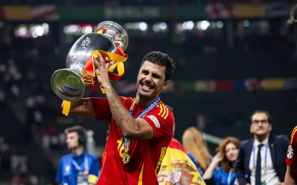 Rodri Hernández celebrates with the trophy after a victory, wearing the Spain National Football Team kit, capturing the joy of the moment in this vibrant 4K Ultra HD wallpaper.
