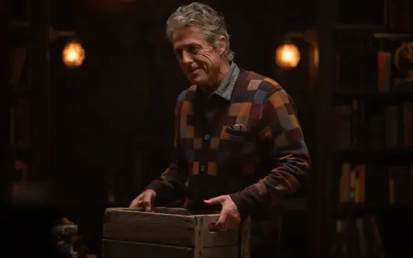 A scene from the movie Heretic (2024) featuring Hugh Grant, showcasing a warm, atmospheric setting with dim lighting and a wooden crate. 4K Ultra HD wallpaper.