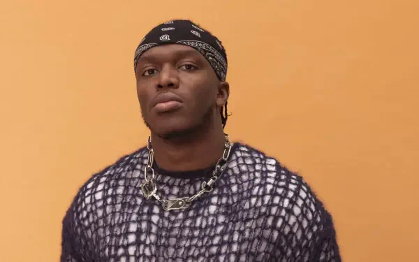 A high-definition desktop wallpaper featuring celebrity KSI, confidently posing against an orange background, wearing a distinctive outfit and accessories.