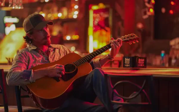 A scene from the TV show Tulsa King, featuring Garrett Hedlund playing acoustic guitar in a vibrant, dimly lit bar, showcasing a lively atmosphere. 4K Ultra HD desktop wallpaper.