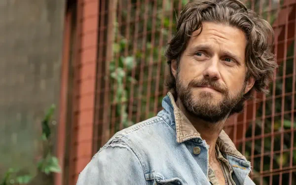 A thoughtful character from the TV show Earth Abides gazes into the distance, set against a rustic backdrop. This HD wallpaper captures a moment of contemplation.