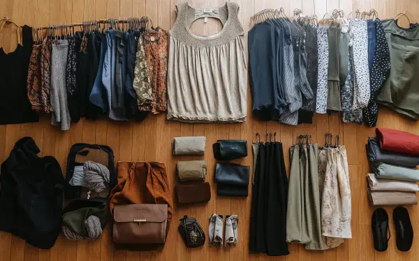 A neatly organized capsule wardrobe displayed on a wooden floor, featuring various tops, pants, and accessories, captured in 4K Ultra HD resolution for a stylish desktop background.