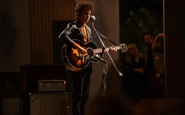 Timothée Chalamet performs with a guitar in a scene from the movie A Complete Unknown. The high-resolution image captures the dynamic atmosphere of the performance.