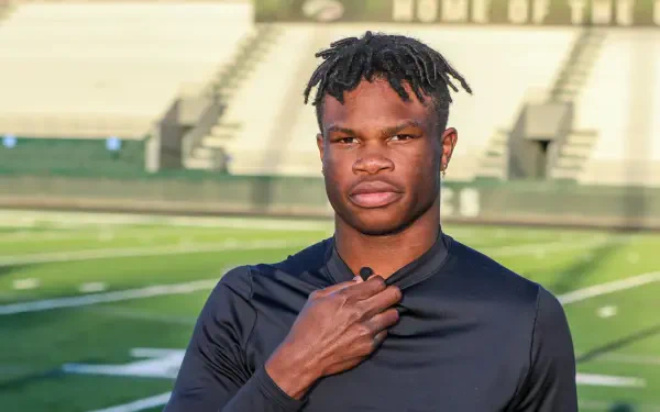 Travis Hunter poses confidently on a football field, wearing a black athletic shirt. This striking image serves as a dynamic 4K Ultra HD desktop wallpaper and background.