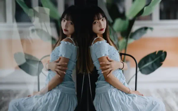 8K Ultra HD PC desktop wallpaper of a woman in a pale blue dress seated by a window, her mirrored reflection on the glass with soft light and large plant leaves in the background.