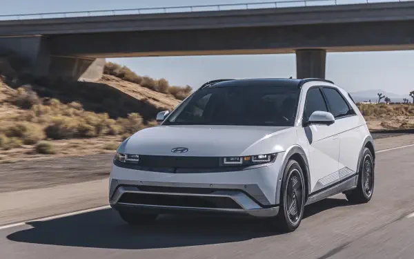 A sleek white Hyundai IONIQ 5 drives along a highway under a bridge, showcasing its modern design. This image serves as a sharp 4K Ultra HD desktop wallpaper.