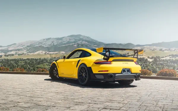Yellow Porsche sports car rear three-quarter view parked on a mountain overlook, scenic valley and peaks in the background — HD PC desktop wallpaper and background.
