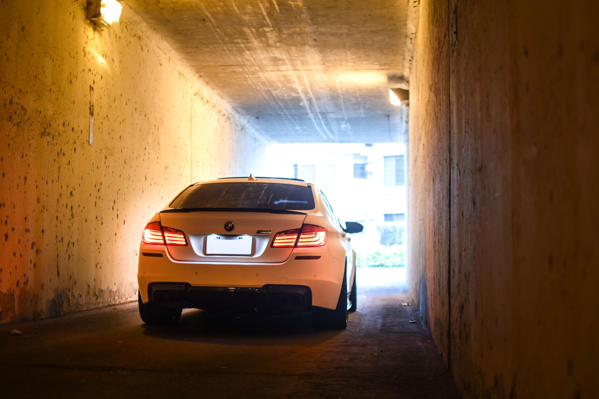 Rear view of a white BMW car exiting a dim concrete tunnel into bright daylight — 5K Ultra HD PC desktop wallpaper.