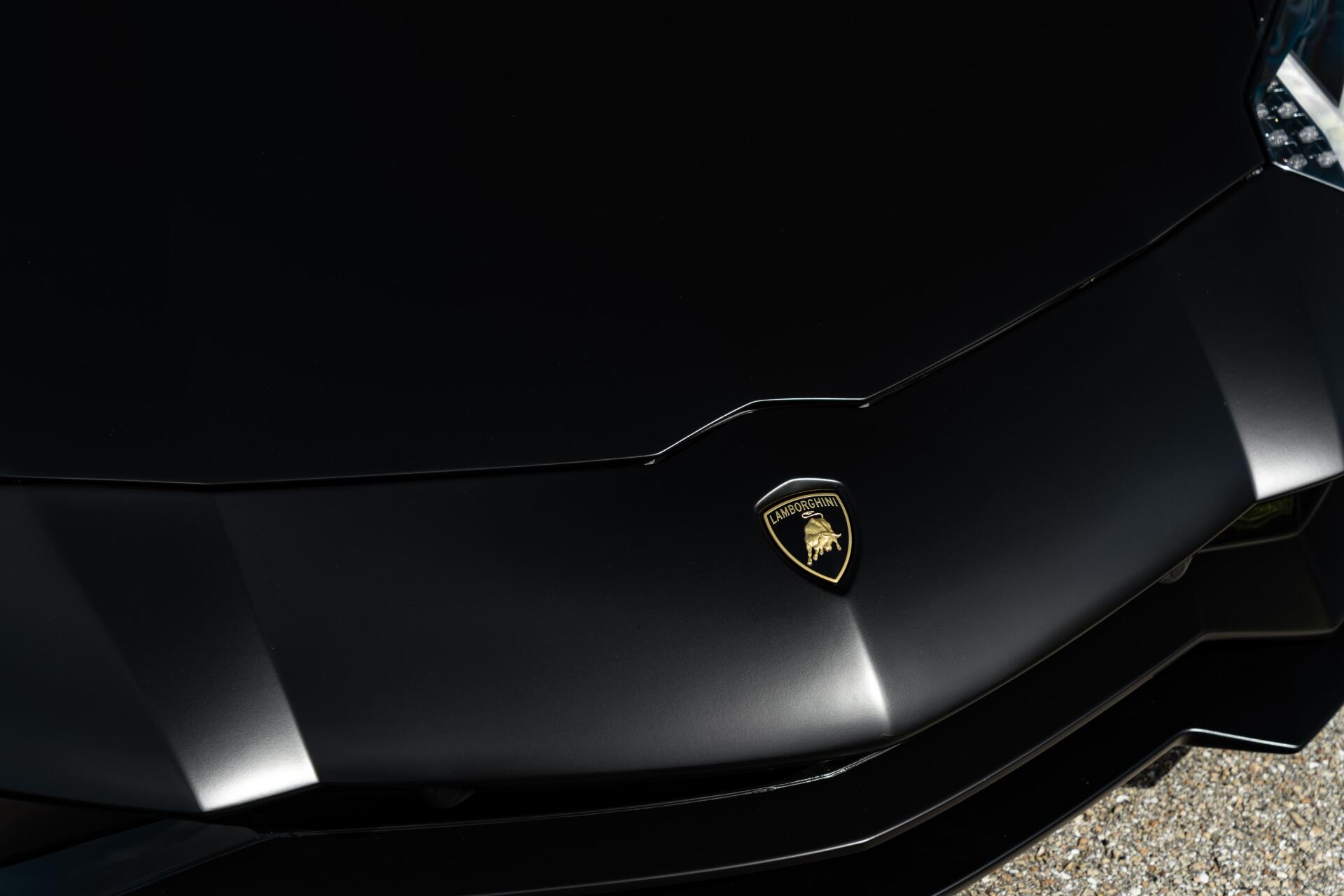 Close-up of a black Lamborghini hood with gold emblem and glossy reflections, high-contrast 8K Ultra HD PC desktop wallpaper background.