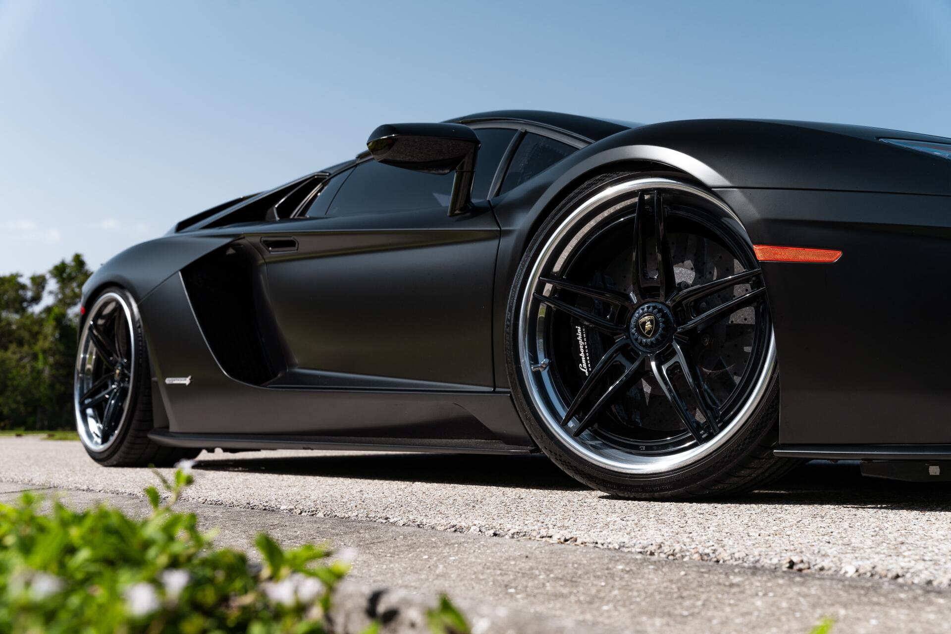 Low-angle 8K Ultra HD PC desktop wallpaper of a black Lamborghini supercar parked on sunlit pavement, close-up on sleek bodywork and glossy alloy wheel.
