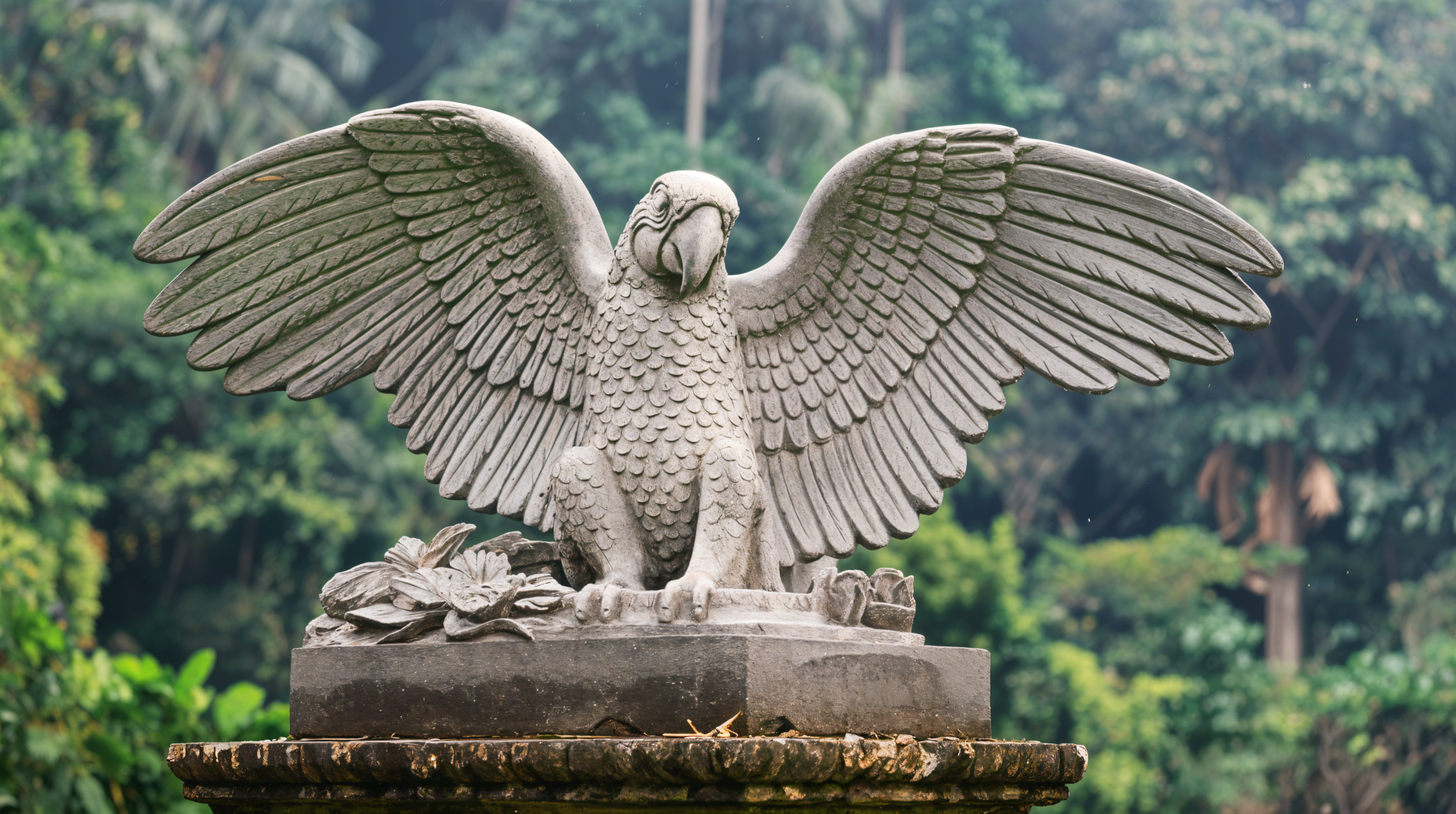 A majestic macaw sculpture with outstretched wings sits atop a pedestal, surrounded by lush greenery, showcased as a stunning 4K Ultra HD desktop wallpaper and background.