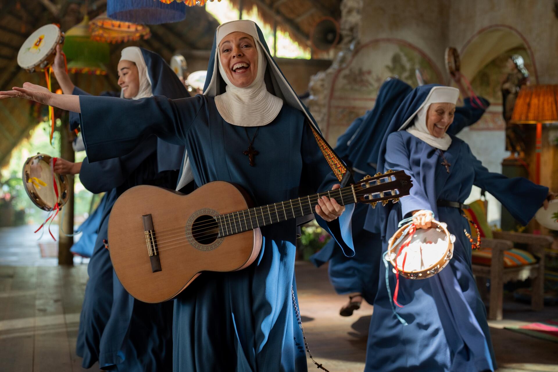 Nuns joyfully play guitar and tambourines inside a rustic setting from the movie Paddington in Peru, featured as an HD PC desktop wallpaper background.