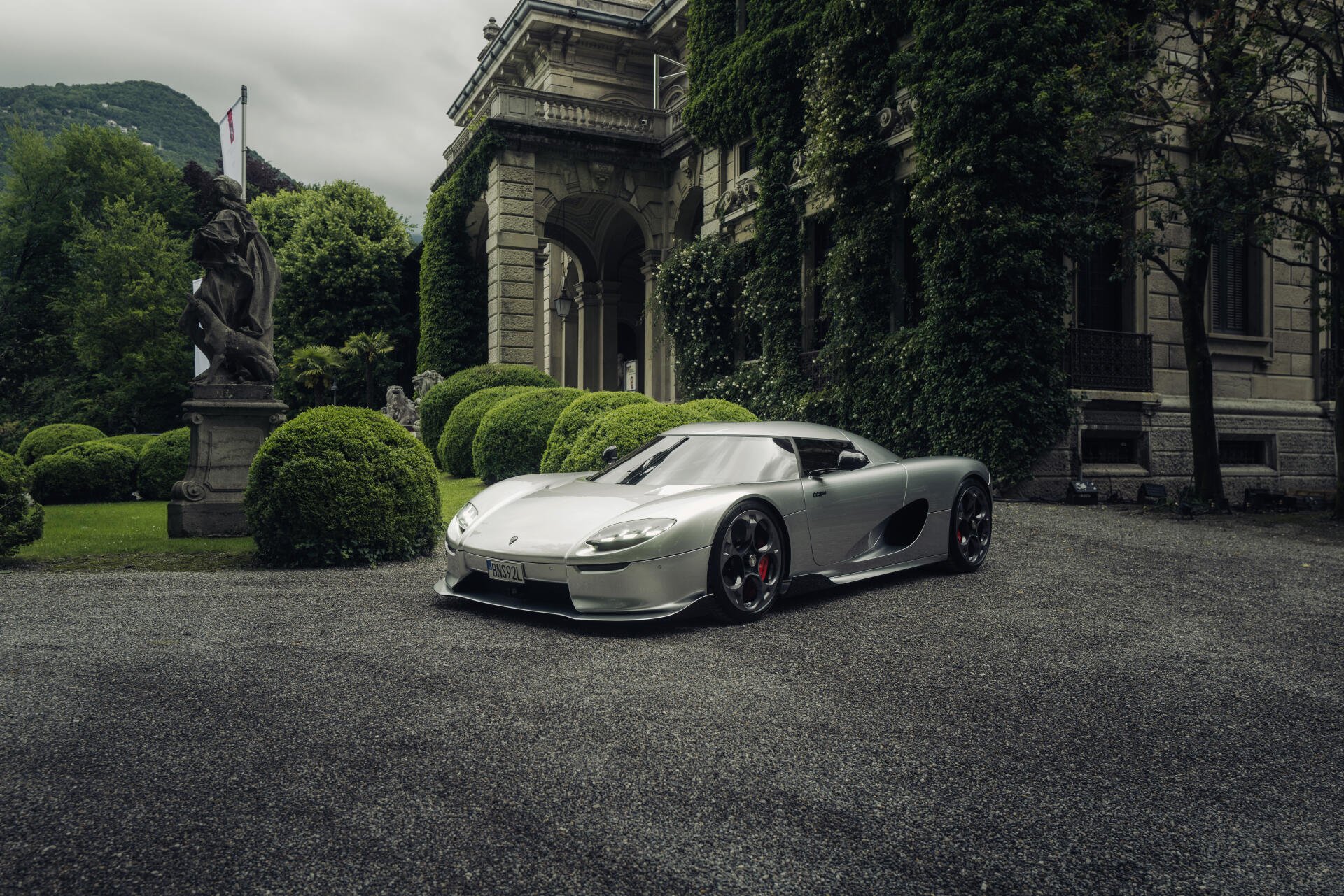 A stunning Koenigsegg CC850 parked in an elegant outdoor setting, showcasing its sleek design against a backdrop of lush greenery and classical architecture. 8K Ultra HD quality.