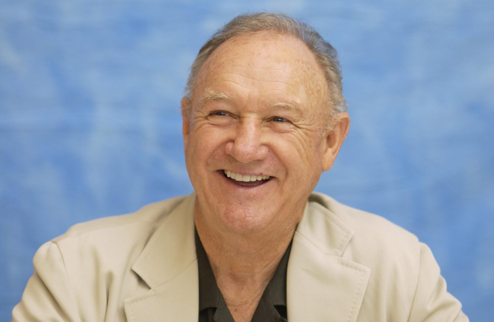 A smiling Gene Hackman, captured in a light-colored suit against a soft blue background. This HD image serves as a vibrant desktop wallpaper.