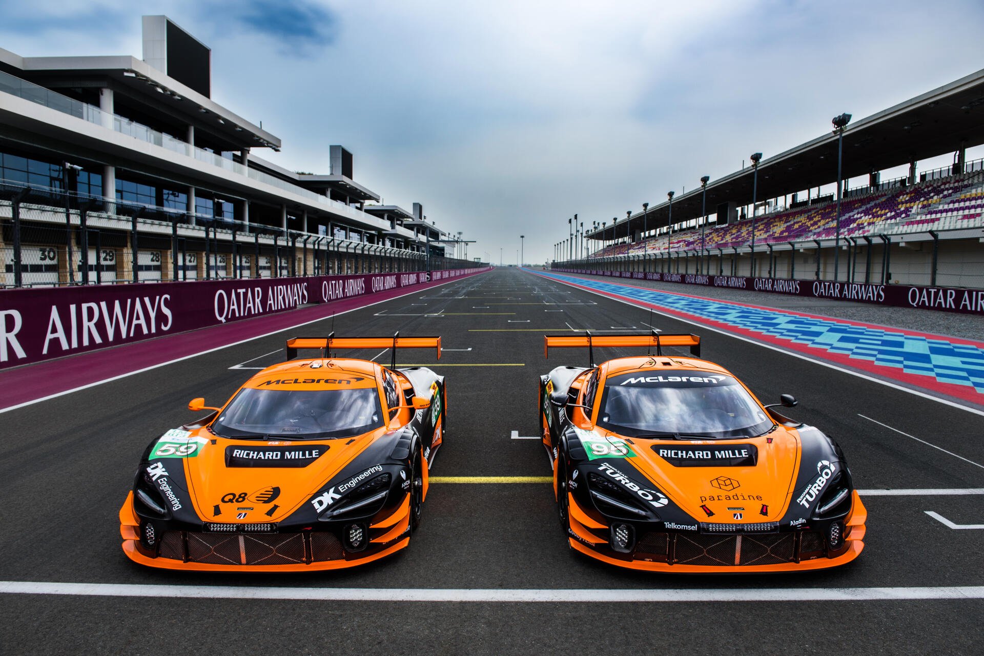 A dynamic 4K Ultra HD image featuring two McLaren GT3 EVO cars lined up on a racetrack, showcasing their striking orange livery against a modern racing backdrop.