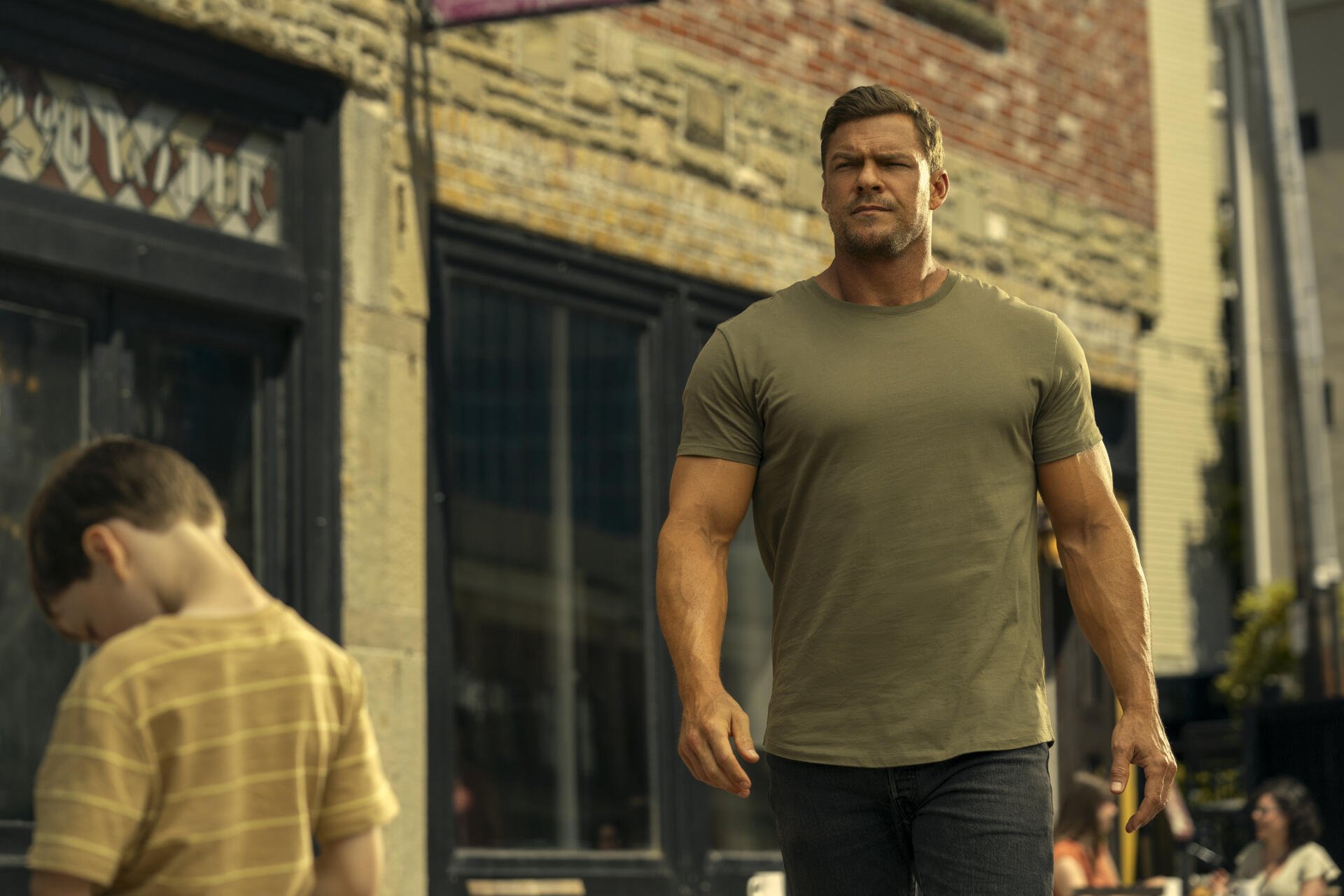 HD desktop wallpaper featuring Alan Ritchson as Reacher from the TV show, walking confidently down a city street.