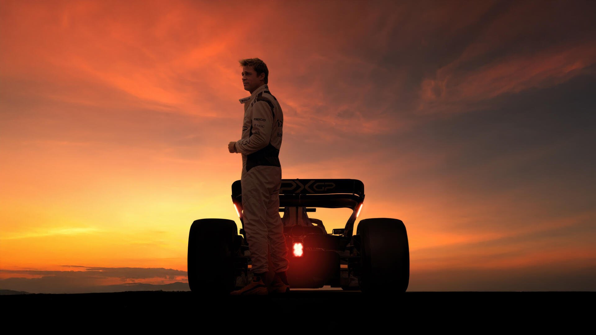 Brad Pitt stands beside an F1 car at sunset in this 8K Ultra HD F1 (2025) desktop wallpaper, capturing a dramatic and cinematic racing moment.