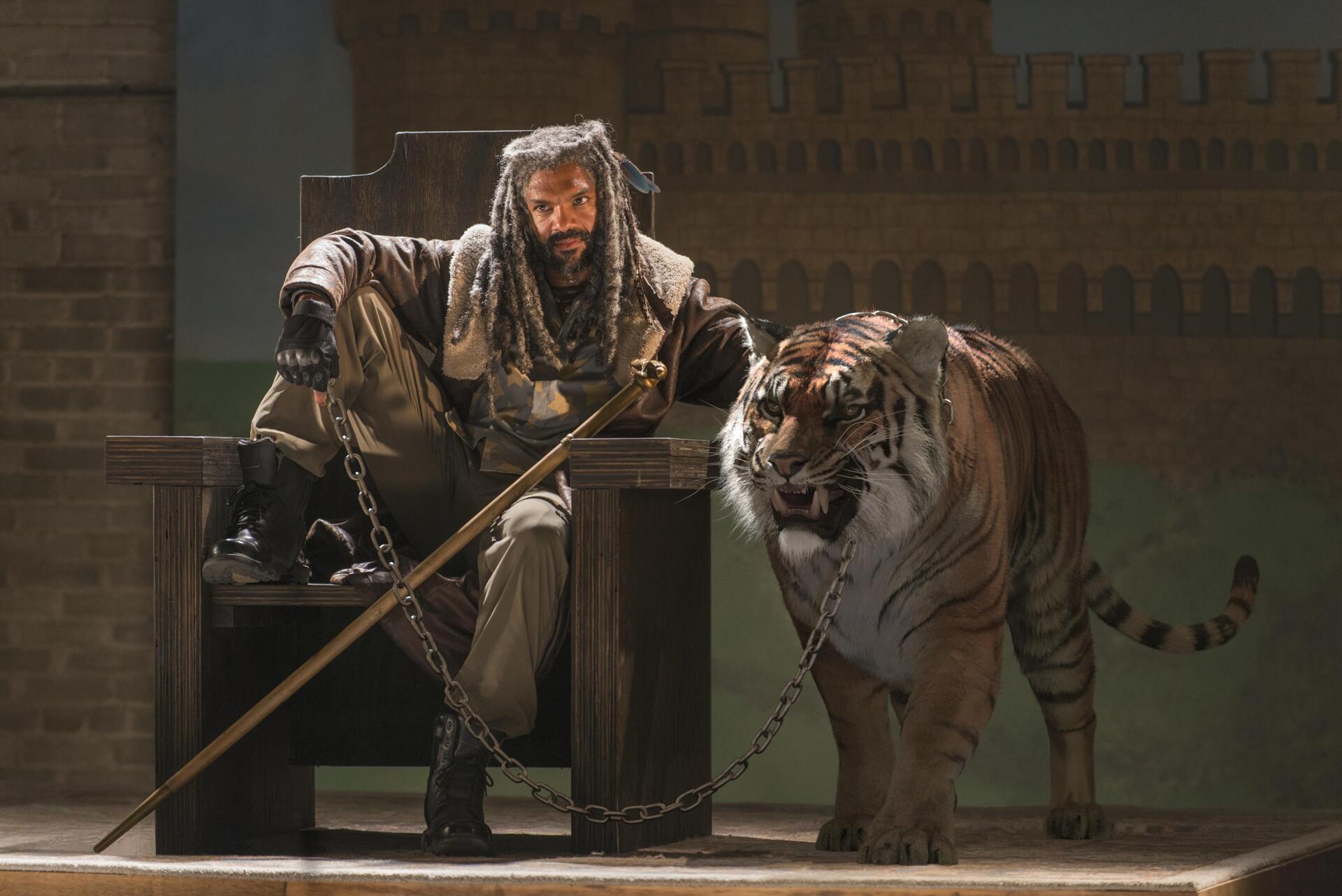 HD PC desktop wallpaper of a character from The Walking Dead seated with a chained tiger, set against a dim, industrial background.