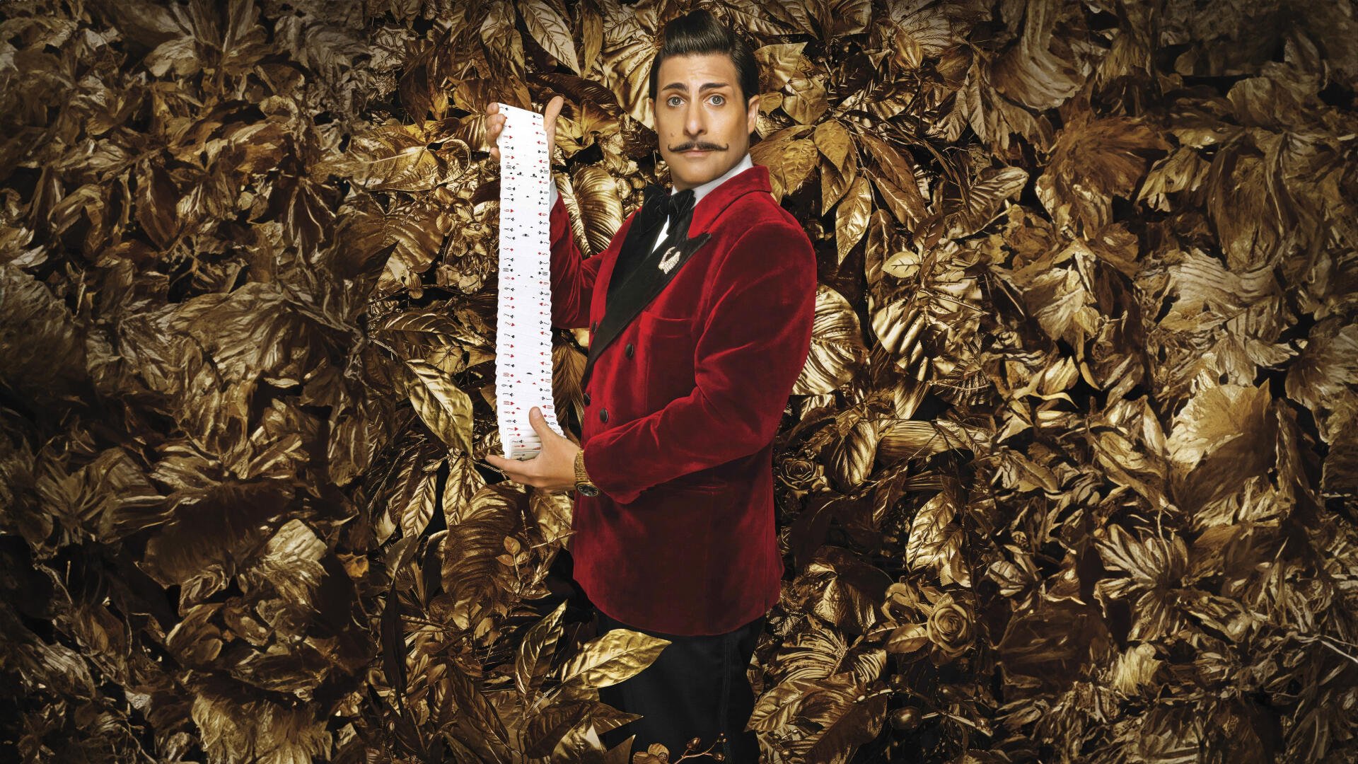8K Ultra HD PC desktop wallpaper for The Hunger Games: The Ballad of Songbirds & Snakes — a man in a red velvet jacket stands among gold leaves holding a long scroll.