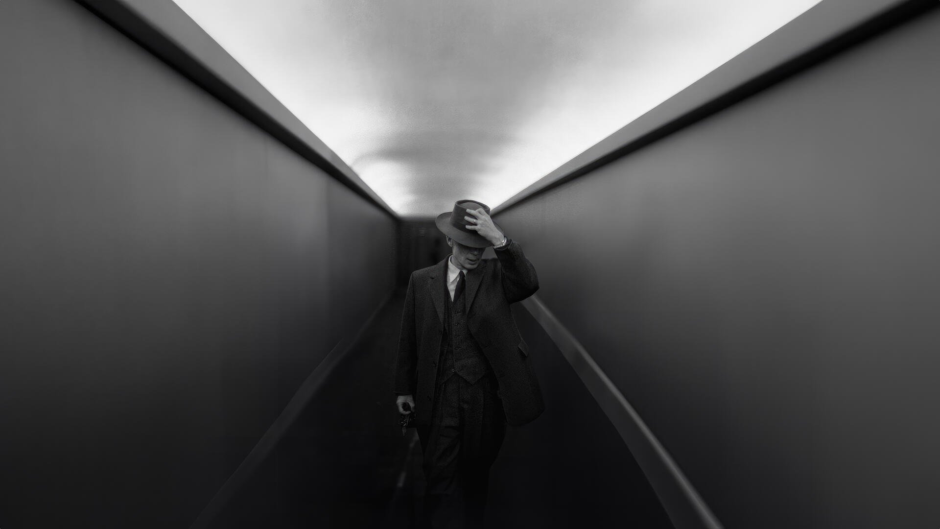 Oppenheimer-tagged 4K Ultra HD PC desktop wallpaper: black-and-white image of a suited man with a briefcase walking a narrow, stark corridor, hand pressed to his forehead.