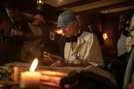 A scene from Paddington in Peru directed by Dougal Wilson, featuring a person examining an old book under candlelight, surrounded by crew members in a dimly lit room.