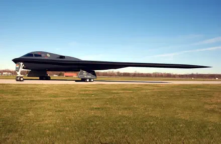 A Northrop Grumman B-2 Spirit aircraft on a grassy runway against a clear blue sky, serving as a striking HD desktop wallpaper and background.