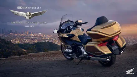 A 25YM Honda GL 1800 Gold Wing motorcycle parked on a scenic overlook, showcasing its sleek design against a backdrop of a city skyline during sunset.