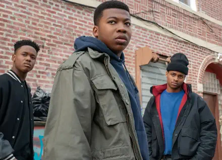 A dramatic scene from the TV show Power Book III: Raising Kanan, featuring three young characters in urban attire, standing against a brick background. Ideal for a HD PC desktop wallpaper.