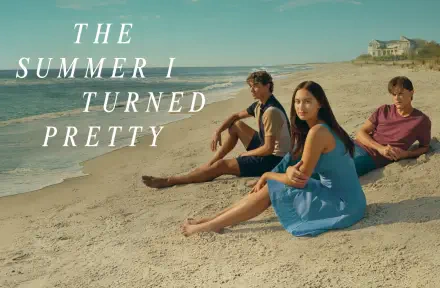 HD desktop wallpaper featuring three characters from the TV show The Summer I Turned Pretty sitting on a sandy beach under a clear sky.