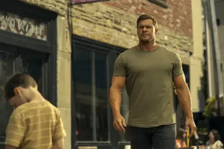 HD desktop wallpaper featuring Alan Ritchson as Reacher from the TV show, walking confidently down a city street.