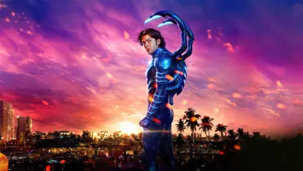 Blue Beetle in glowing sci‑fi armor stands on a rooftop at sunset, city skyline and palm trees below; vibrant 4K Ultra HD desktop wallpaper with neon purple and orange sky.