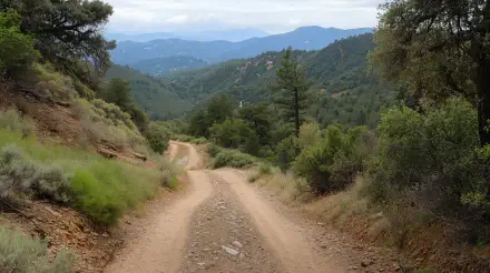 4K Ultra HD PC desktop wallpaper and background of an OHV trail: winding dirt road through green foothills and pines, distant mountains fading into blue haze under a cloudy sky.