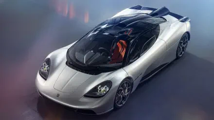 Silver Gordon Murray Automotive hypercar with glass canopy and orange seats, three-quarter top view on an HD PC desktop wallpaper background.