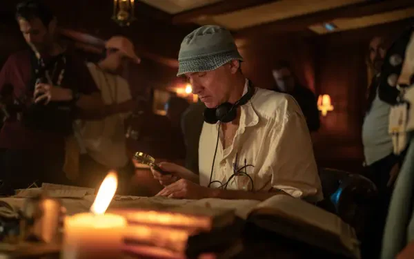 A scene from Paddington in Peru directed by Dougal Wilson, featuring a person examining an old book under candlelight, surrounded by crew members in a dimly lit room.