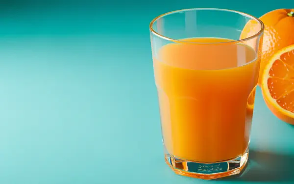 A refreshing glass of orange juice sits on a teal background, accompanied by a halved orange, creating a vibrant 4K Ultra HD desktop wallpaper.