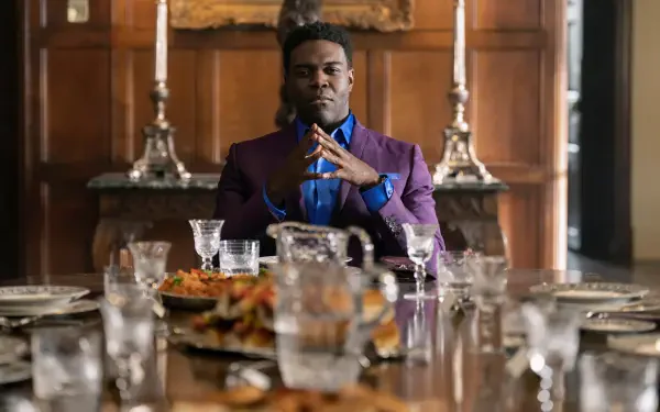 A still from the TV show Ted Lasso, featuring Sam Richardson seated at an elegant dining table, exuding confidence, surrounded by dishes and glasses. 8K Ultra HD quality background.