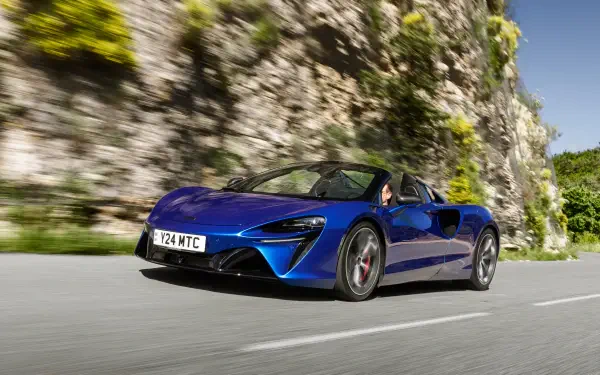 A stunning blue McLaren Artura speeds along a scenic road, showcasing its sleek design against a backdrop of rocky terrain, perfect for a 4K Ultra HD desktop wallpaper.