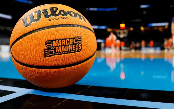 HD PC desktop wallpaper featuring a close-up of an NCAA March Madness Wilson basketball on a court, with blurred players and arena lights in the background.