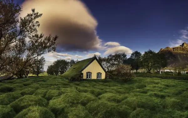 HD desktop wallpaper of an Icelandic landscape featuring a grass-covered cottage near a cemetery and church under a dramatic sky.