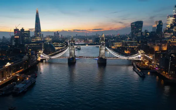 Cityscape of London at dusk featuring Tower Bridge illuminated over the Thames, surrounded by skyscrapers in a 4K Ultra HD desktop wallpaper background.