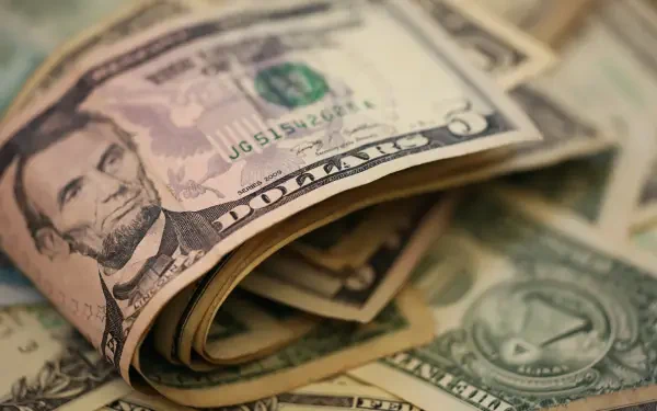 Close-up HD desktop wallpaper featuring a rolled US dollar bill with Abraham Lincoln's portrait, surrounded by additional scattered currency notes.