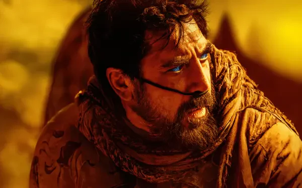 Dune: Part Two — 4K Ultra HD PC desktop wallpaper of a bearded man in weathered desert robes with blue eye paint, sand-blurred background and warm golden light.