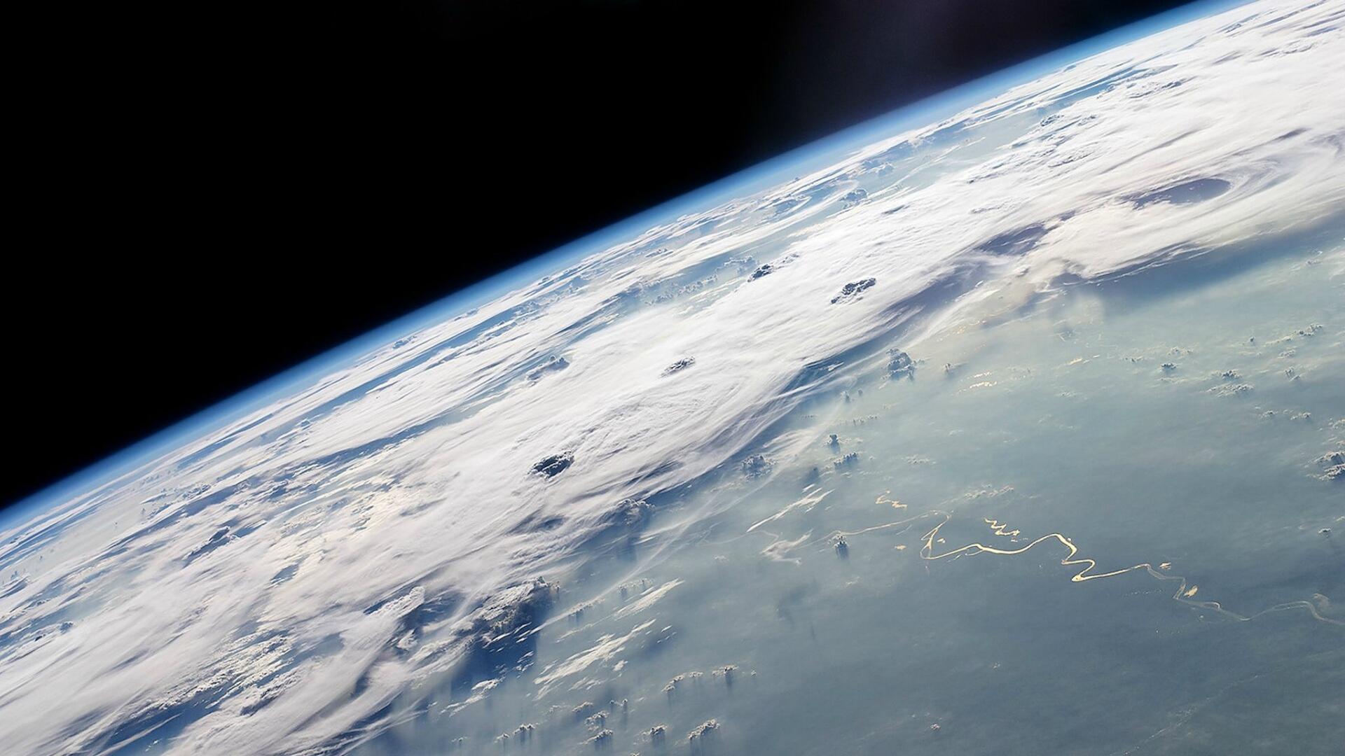 HD PC desktop wallpaper showing a planet's curved, cloud-swept horizon from orbit against the blackness of space.