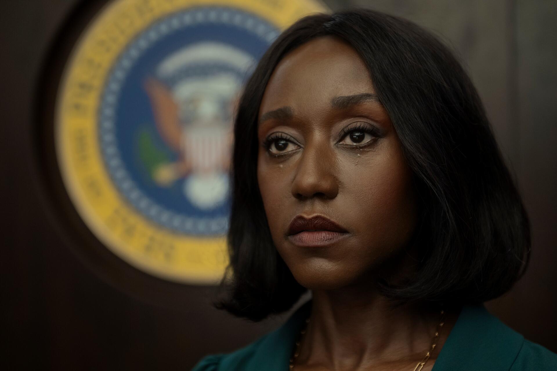 Close-up of a tearful character from the TV drama The Diplomat, solemn gaze with an official seal behind her — 2K Quad HD PC desktop wallpaper.